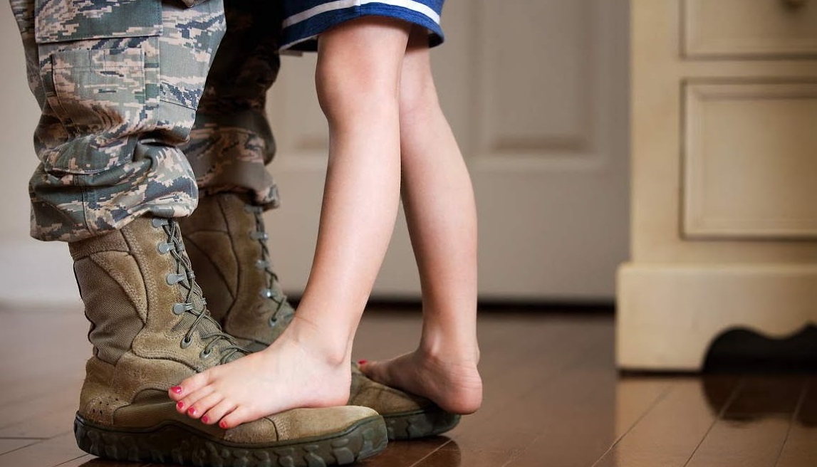 Person in military uniform embracing someone in civilian clothes standing on their boots